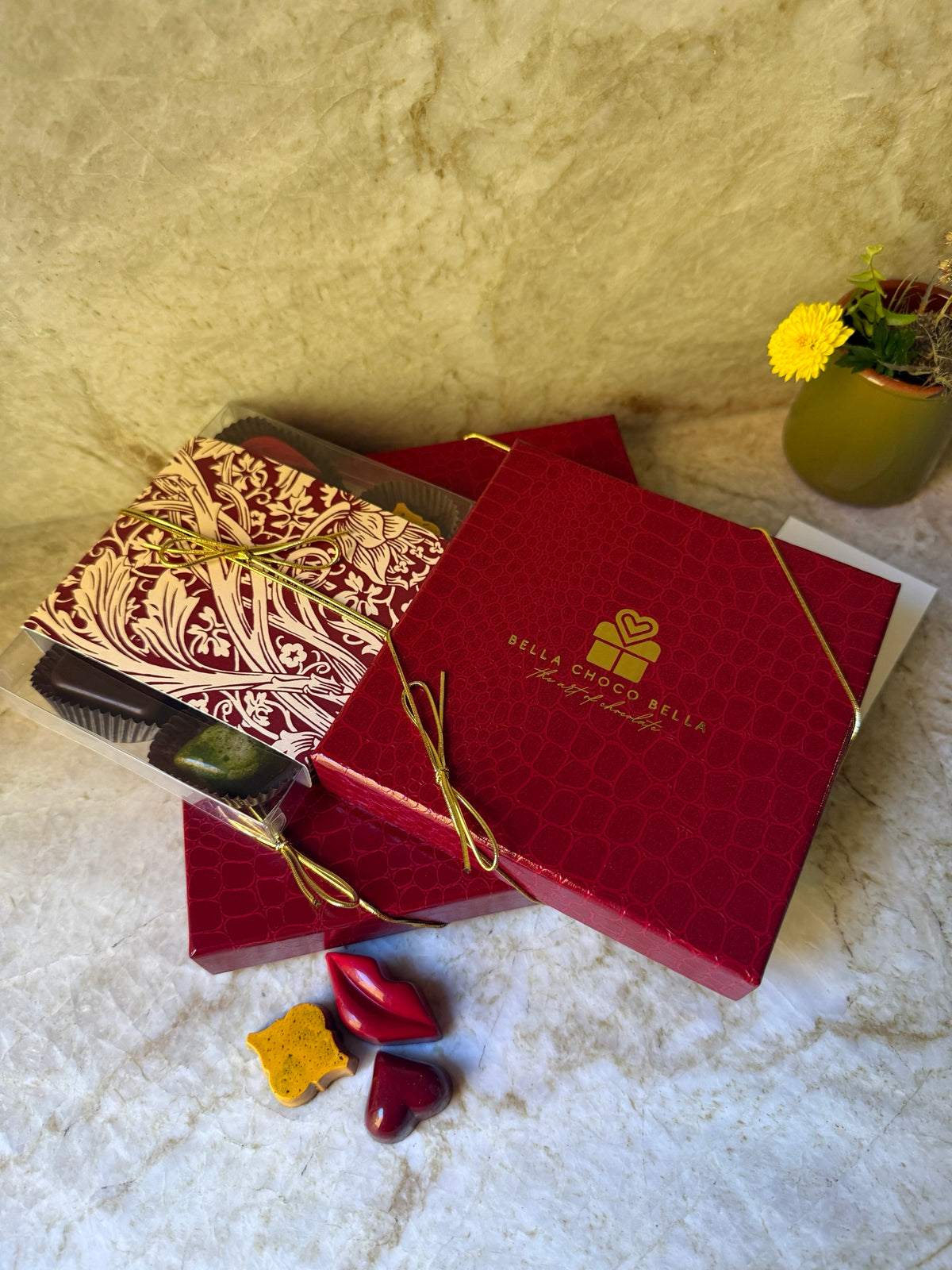 Hand-painted chocolate lips, heart and gold bonbon in front of stacked red gift boxes